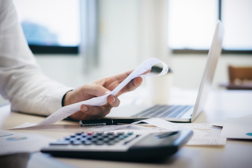 inadimplência na pandemia - pessoa segurando um papel, em uma mesa com calculadora e notebook